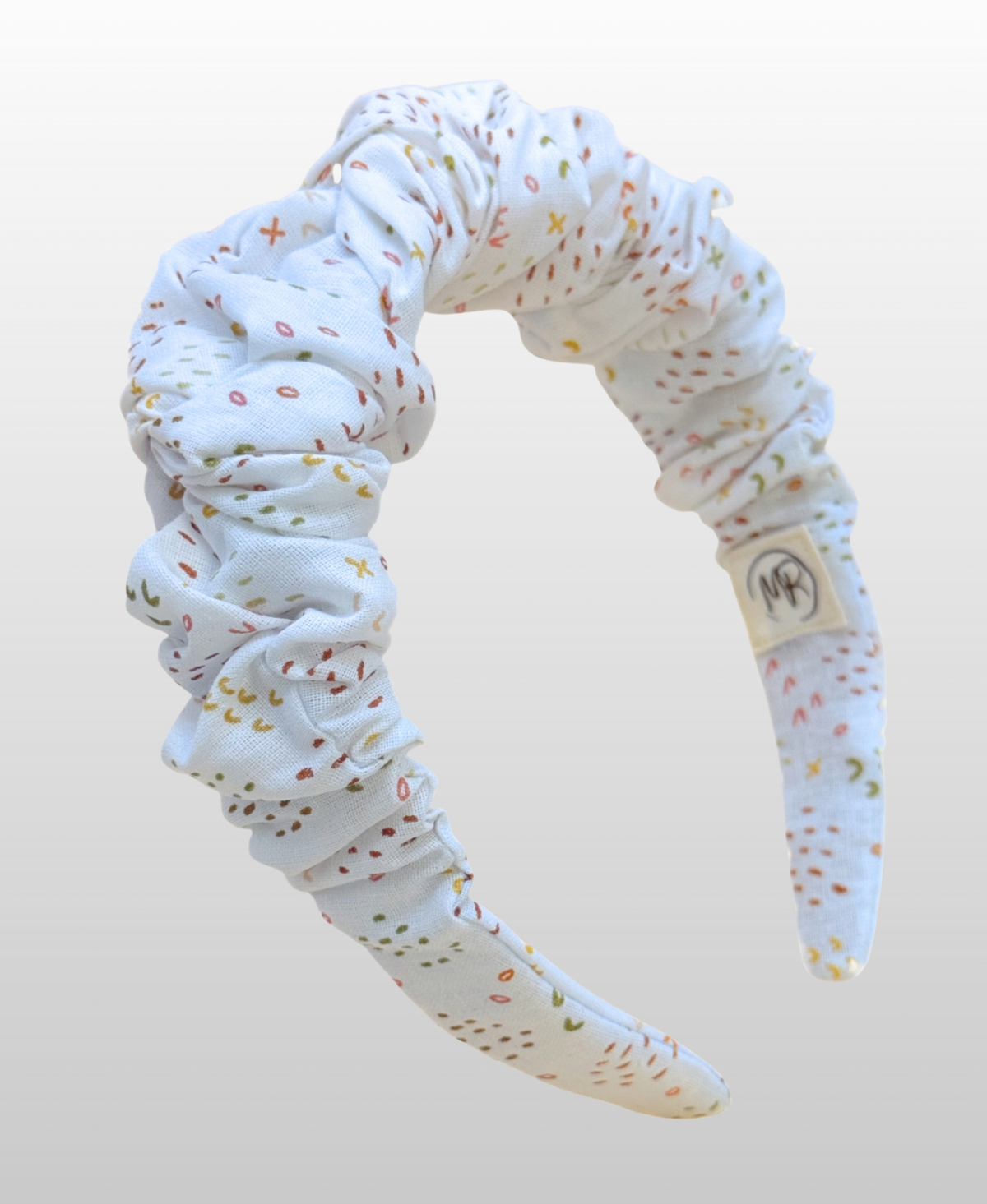 Serre-tête au tissu doux à fond blanc, parsemé d'un délicat motif de confettis multicolores.