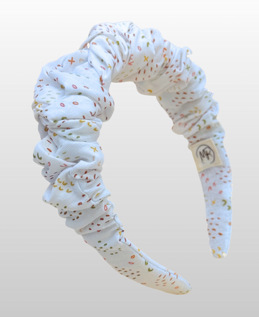 Serre-tête au tissu doux à fond blanc, parsemé d'un délicat motif de confettis multicolores.