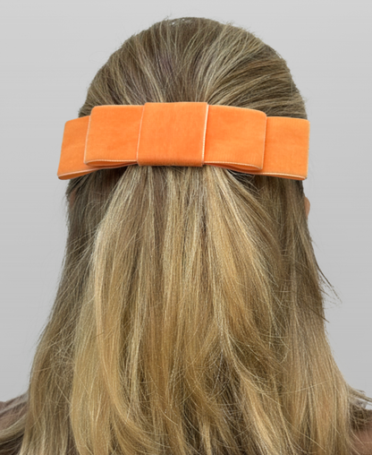 Nœud minimaliste d'une teinte orange vif, porté en demi-queue sur une chevelure blonde. 