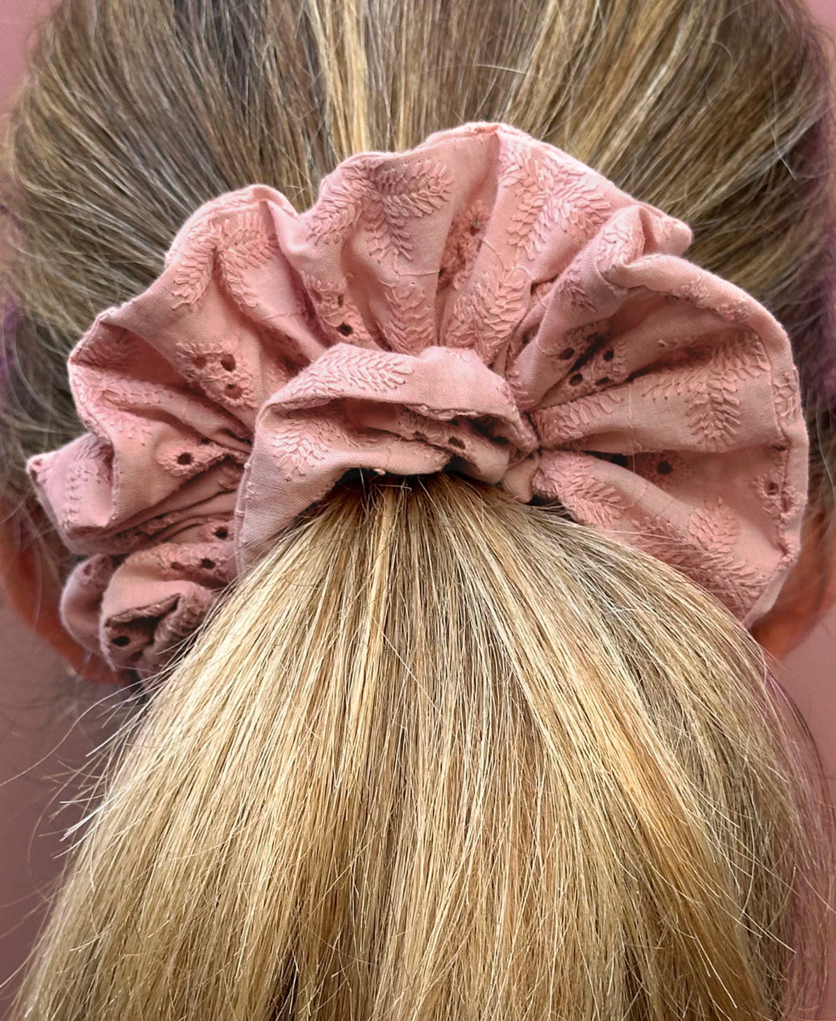 Chouchou Eva en broderie anglaise rose poudré porté en queue de cheval sur femme blonde.