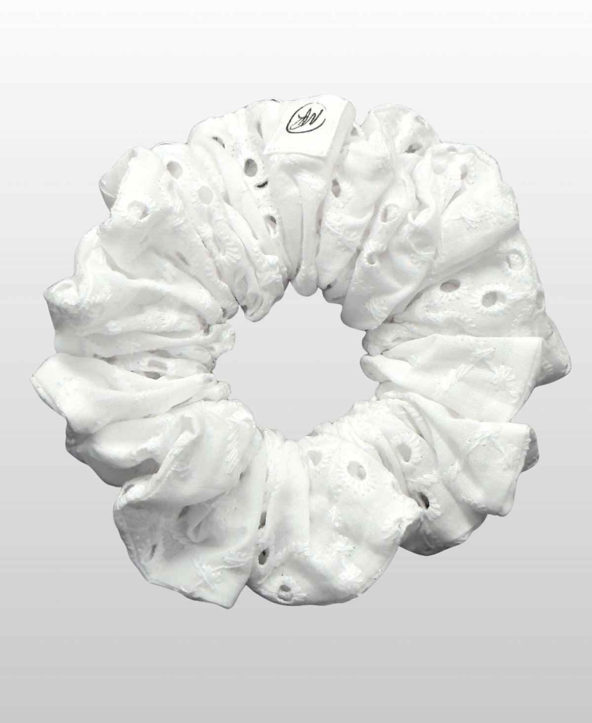 Chouchou confectionné en broderie anglaise 100 % coton dans une teinte blanche neutre, avec des perforations et des motifs floraux brodés.