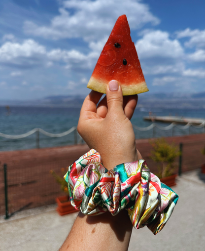 Chouchou en soie italienne aux teintes fraîches et lumineuses de rose pastèque, rouge corail, vert et turquoise, sur un fond ivoire, porté au poignet.