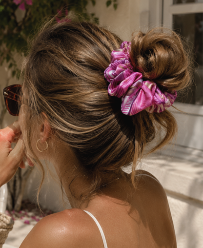 Chouchou en satin de soie fuchsia, porté sur un chignon haut coiffé-décoiffé. [IA]