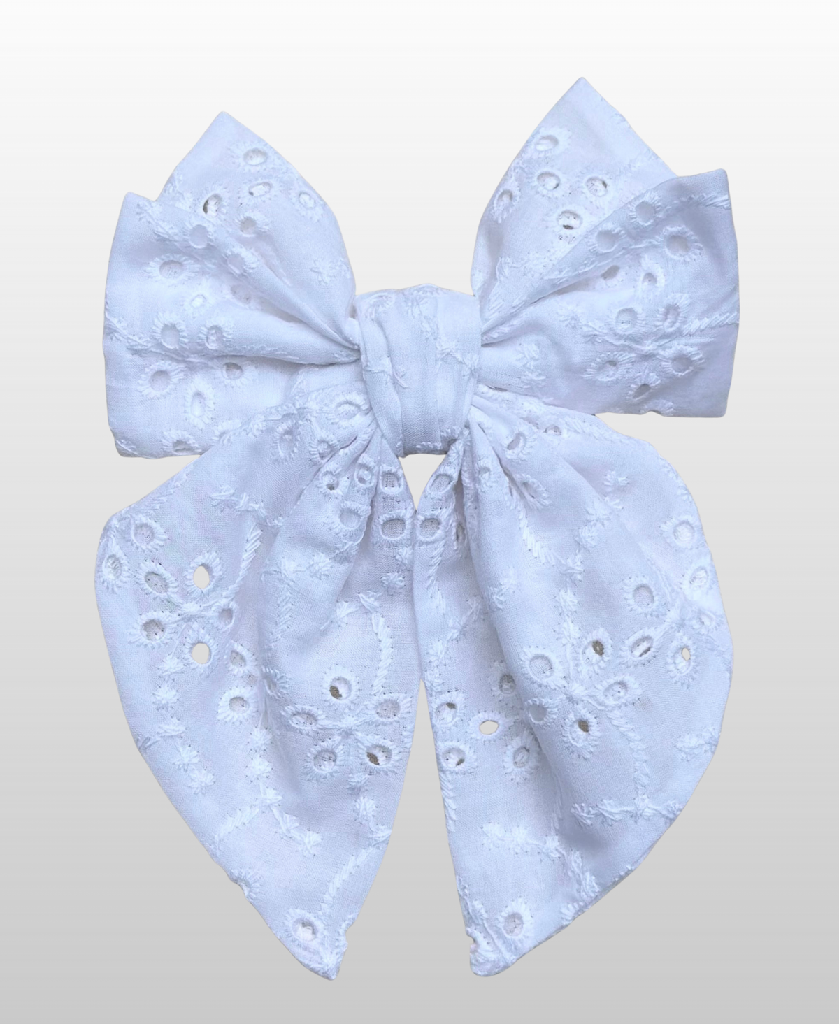 Montée sur une barrette dorée à l’or fin, le nœud Melis est fabriqué en broderie anglaise blanche.