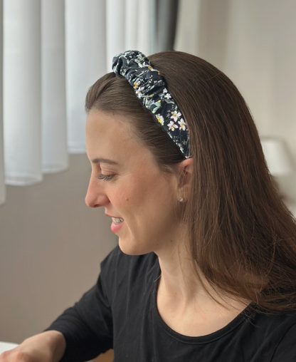 Une jeune femme brune porte le serre-tête Nérolia à l'imprimé fleuri, confortablement installée chez elle.