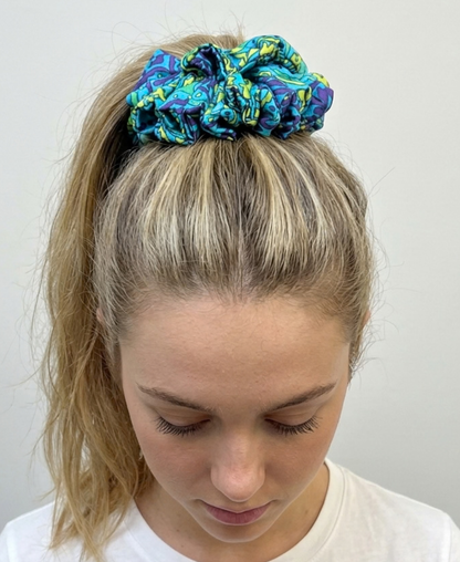 Chouchou en satin de soie bleu turquoise, avec des touches de violet et de vert anis porté en queue de cheval haute.